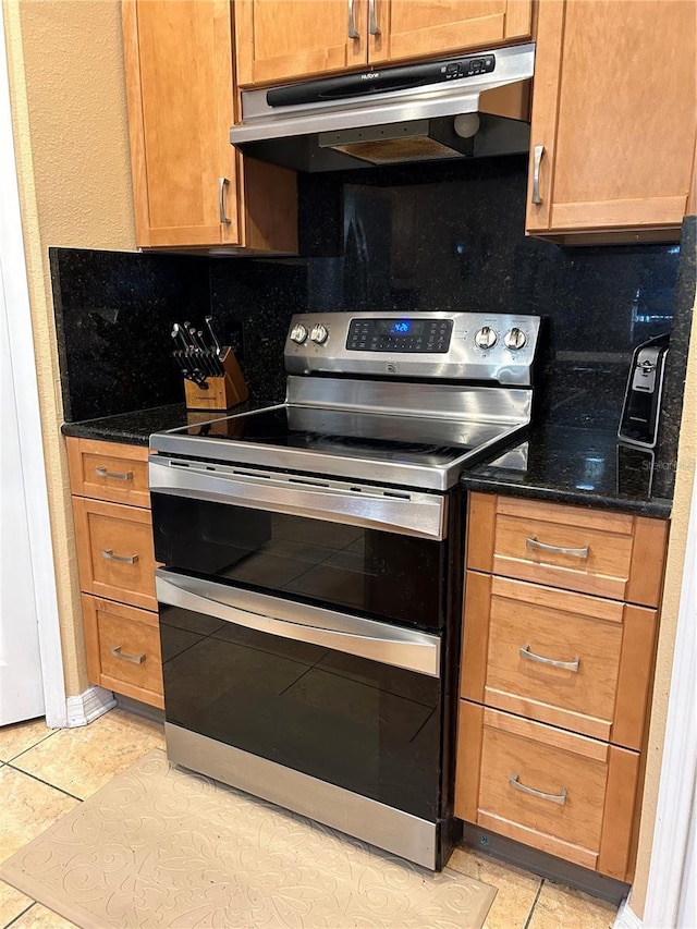 kitchen featuring under cabinet range hood, tasteful backsplash, light tile patterned floors, and range with two ovens