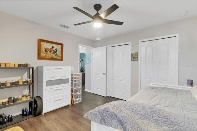 bedroom featuring a ceiling fan, dark wood-style flooring, visible vents, and multiple closets