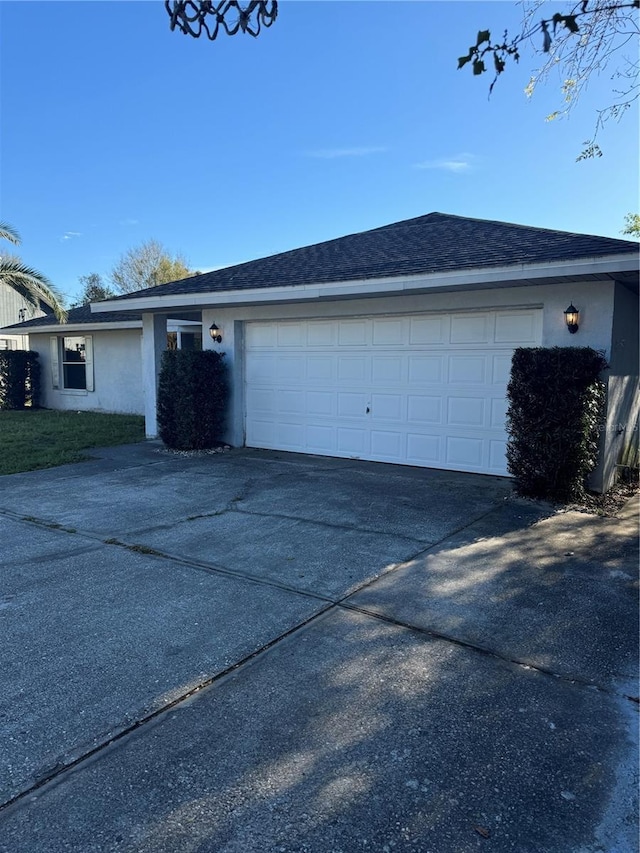 view of front of property with an attached garage, roof with shingles, concrete driveway, and stucco siding