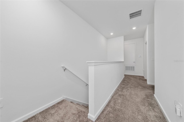 hallway with an upstairs landing, visible vents, carpet floors, and baseboards