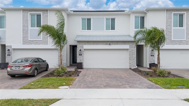 townhome / multi-family property featuring a garage, stone siding, driveway, and stucco siding