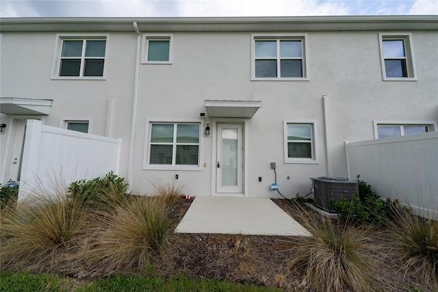 rear view of house with central air condition unit, stucco siding, and fence