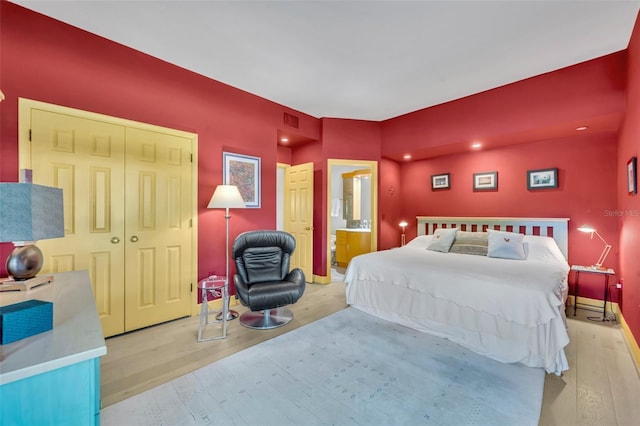 bedroom with ensuite bath, wood finished floors, visible vents, and baseboards