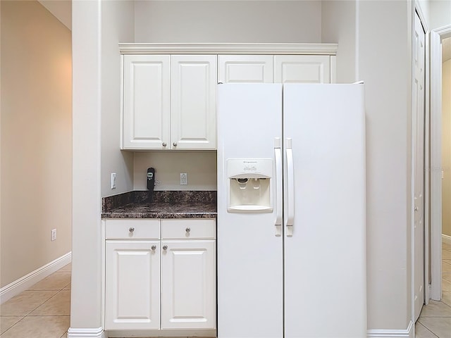 kitchen featuring light tile patterned floors, baseboards, white fridge with ice dispenser, and white cabinetry