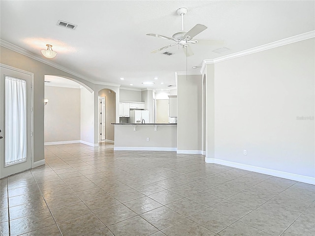 unfurnished living room featuring a ceiling fan, arched walkways, crown molding, and baseboards