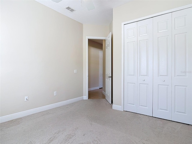 unfurnished bedroom featuring ceiling fan, light colored carpet, visible vents, baseboards, and a closet