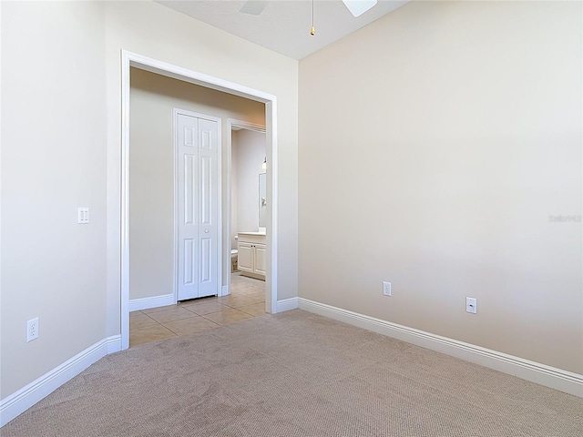 empty room with light carpet, ceiling fan, baseboards, and light tile patterned flooring