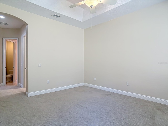 spare room featuring arched walkways, light carpet, visible vents, and baseboards