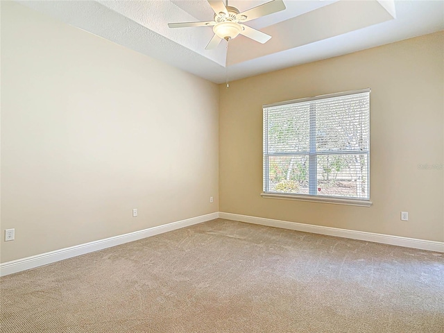 unfurnished room featuring a raised ceiling, light carpet, ceiling fan, and baseboards