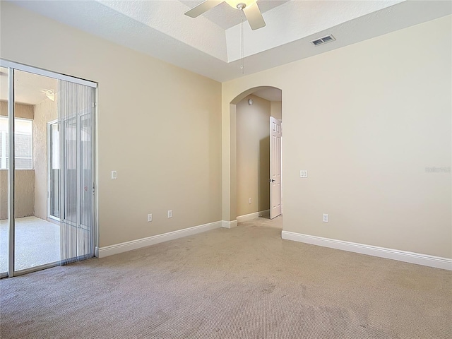 unfurnished room with arched walkways, ceiling fan, light colored carpet, visible vents, and baseboards