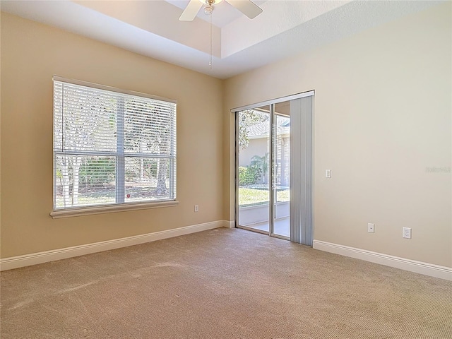 carpeted spare room featuring a raised ceiling, ceiling fan, and baseboards