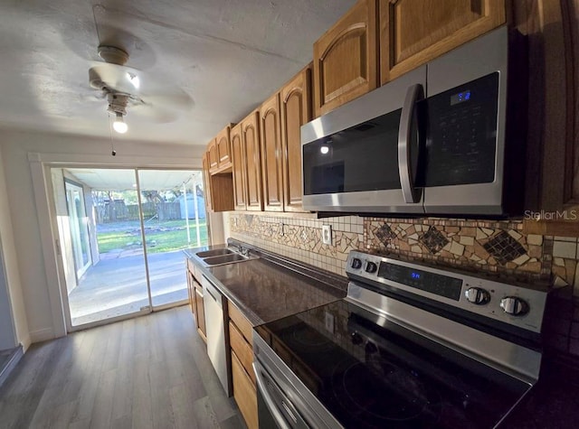 kitchen featuring stainless steel appliances, dark countertops, backsplash, a sink, and wood finished floors