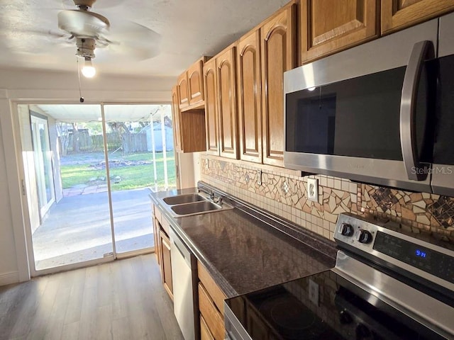 kitchen featuring dark countertops, decorative backsplash, appliances with stainless steel finishes, a sink, and light wood-type flooring