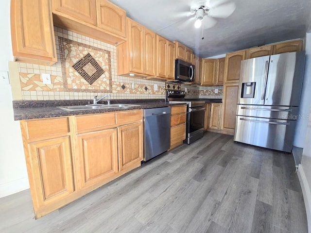 kitchen featuring stainless steel appliances, a sink, light wood-style floors, decorative backsplash, and dark countertops