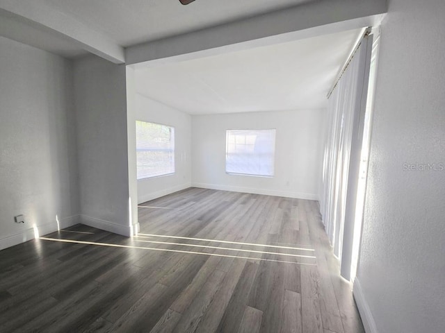 spare room featuring wood finished floors, beam ceiling, and baseboards