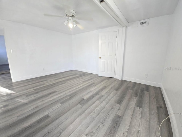 empty room featuring a ceiling fan, wood finished floors, visible vents, and baseboards