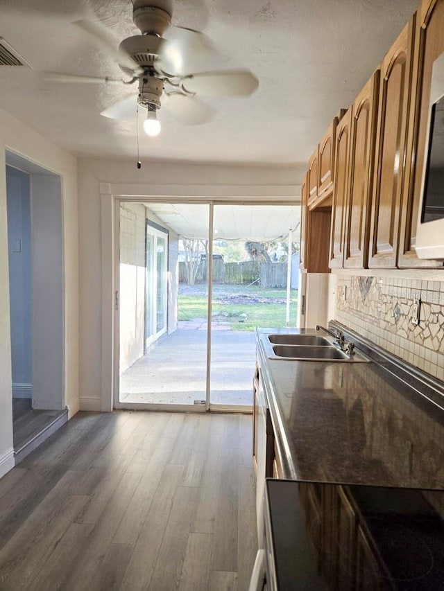 kitchen featuring decorative backsplash, a ceiling fan, wood finished floors, dark countertops, and a sink