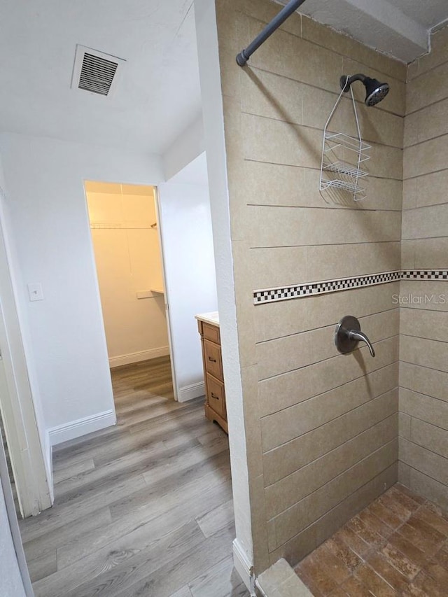 full bath with visible vents, vanity, wood finished floors, a walk in closet, and a stall shower