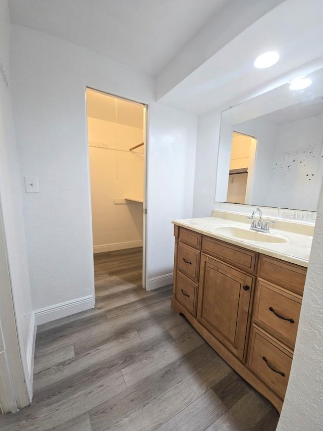 bathroom with vanity, baseboards, wood finished floors, and a walk in closet