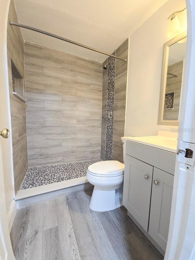 bathroom featuring vanity, toilet, wood finished floors, and a stall shower
