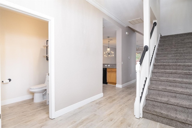 staircase with baseboards, wood finished floors, visible vents, and a notable chandelier