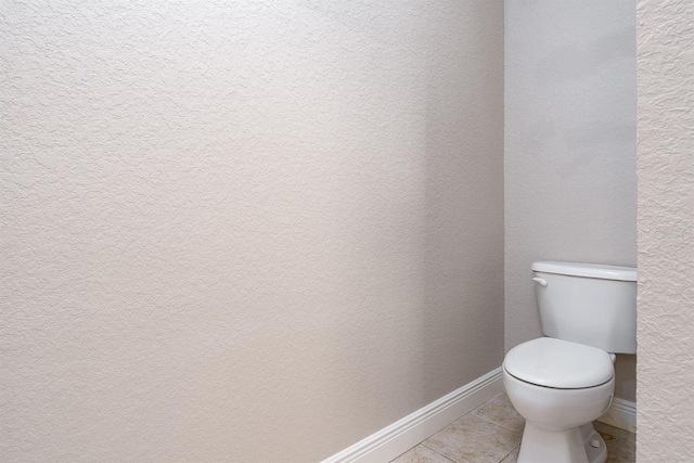 bathroom with toilet, a textured wall, baseboards, and tile patterned floors