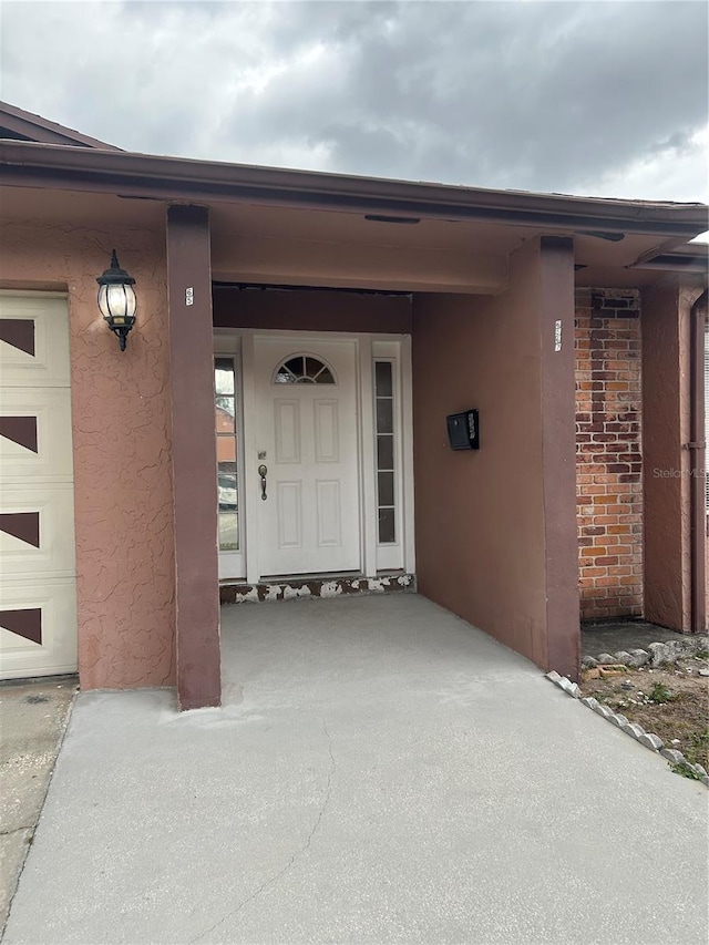 doorway to property with a garage, brick siding, and stucco siding