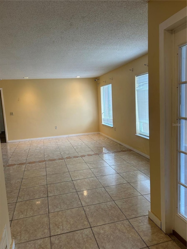 empty room with visible vents, a textured ceiling, baseboards, and light tile patterned floors