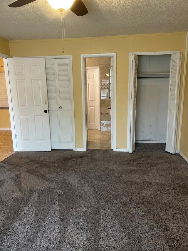 unfurnished bedroom featuring a textured ceiling, carpet floors, a ceiling fan, baseboards, and two closets