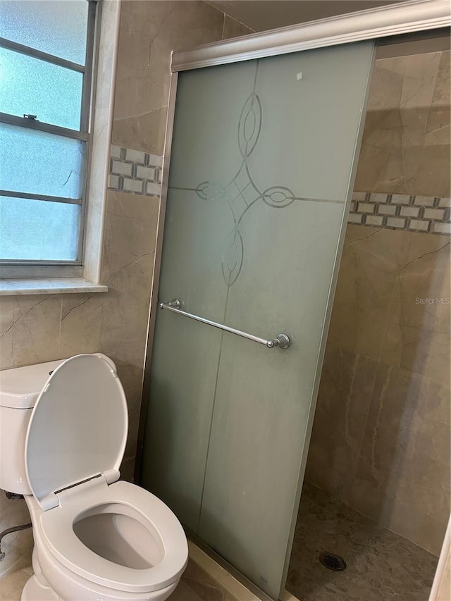 bathroom with a stall shower, tile walls, and toilet