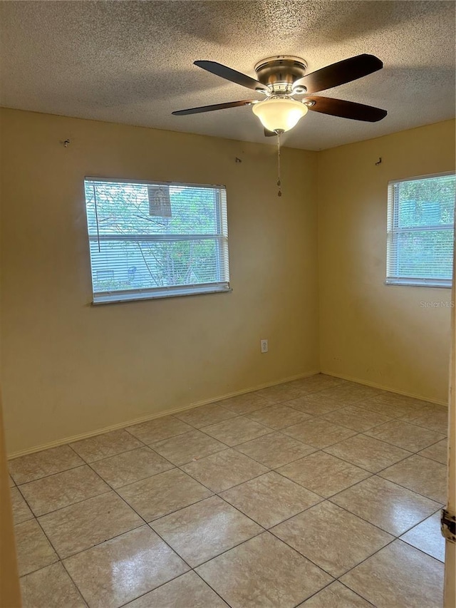 unfurnished room with a textured ceiling, ceiling fan, light tile patterned floors, and baseboards