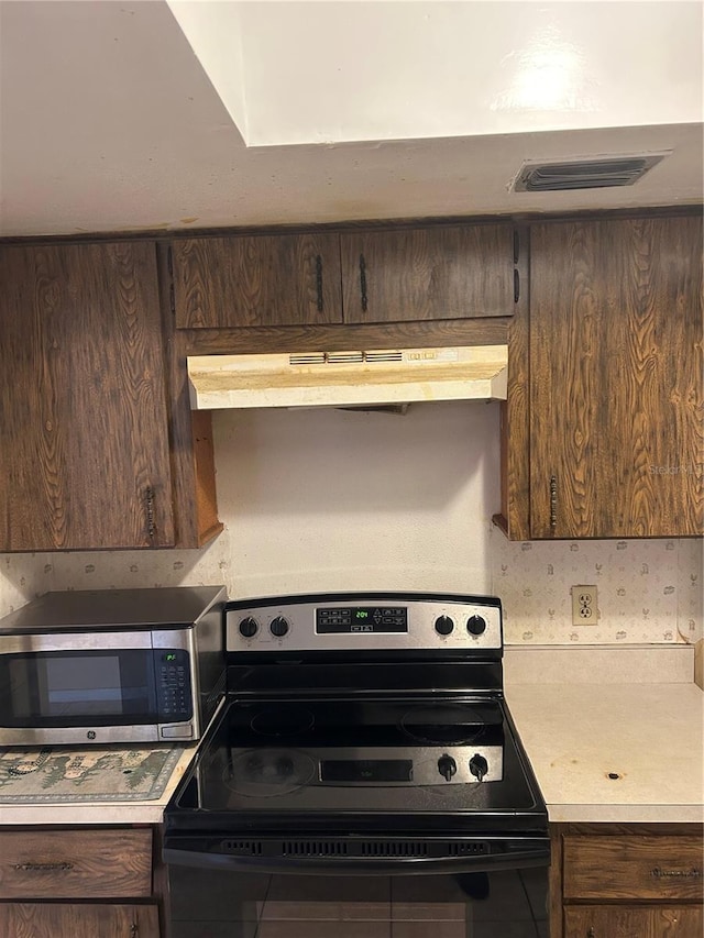 kitchen with black range with electric cooktop, under cabinet range hood, visible vents, light countertops, and stainless steel microwave