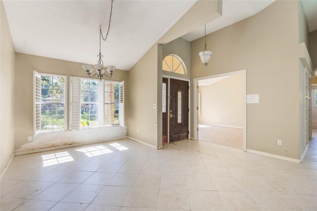 tiled entryway with a notable chandelier, a textured ceiling, baseboards, and a towering ceiling