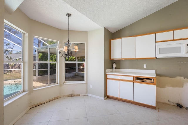 kitchen featuring white microwave, light countertops, lofted ceiling, hanging light fixtures, and white cabinets