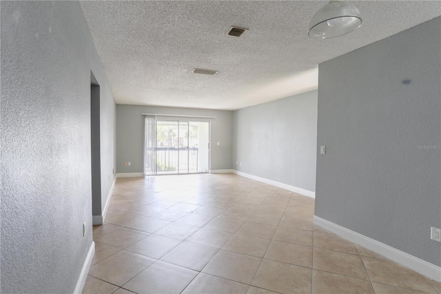 tiled empty room with visible vents, baseboards, a textured ceiling, and a textured wall