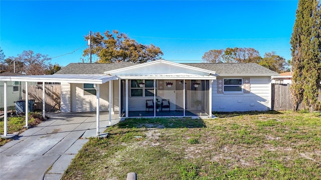 back of house featuring concrete driveway, a sunroom, fence, a yard, and brick siding