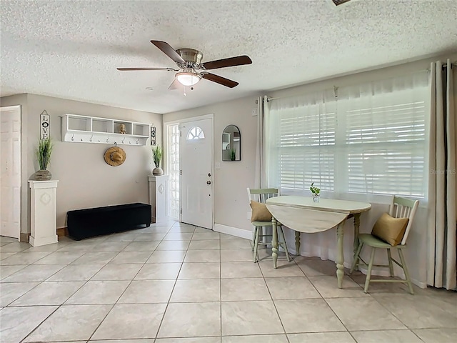 foyer with a textured ceiling, light tile patterned flooring, a ceiling fan, and baseboards