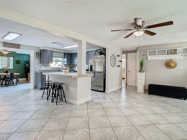 kitchen featuring light tile patterned floors, stainless steel fridge, a ceiling fan, gray cabinets, and light countertops