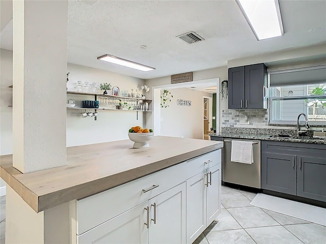 kitchen featuring light tile patterned floors, visible vents, backsplash, a sink, and dishwasher