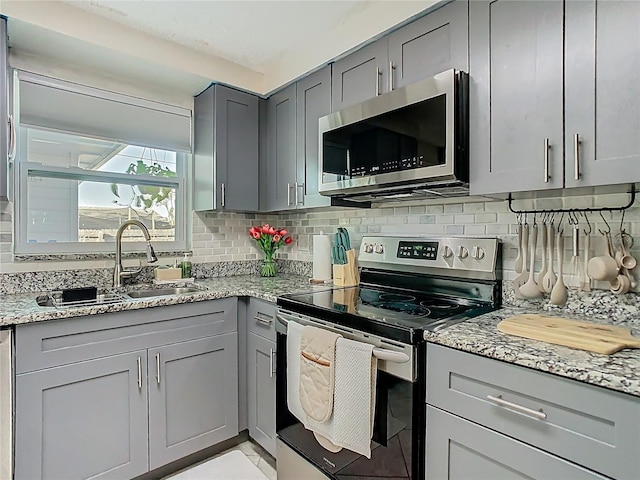 kitchen featuring tasteful backsplash, appliances with stainless steel finishes, gray cabinets, and a sink