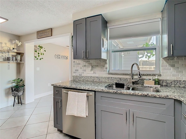 kitchen with light tile patterned floors, light stone counters, gray cabinetry, a sink, and stainless steel dishwasher