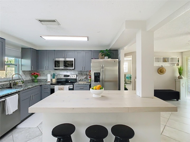 kitchen with stainless steel appliances, a breakfast bar, a sink, gray cabinets, and tasteful backsplash