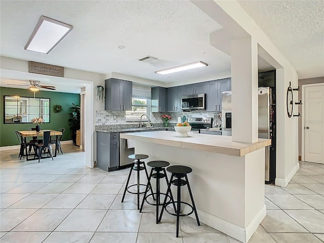 kitchen with stainless steel appliances, visible vents, gray cabinetry, light tile patterned flooring, and a kitchen bar