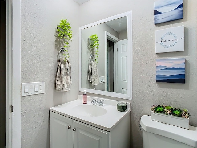 bathroom featuring a textured wall, vanity, and toilet