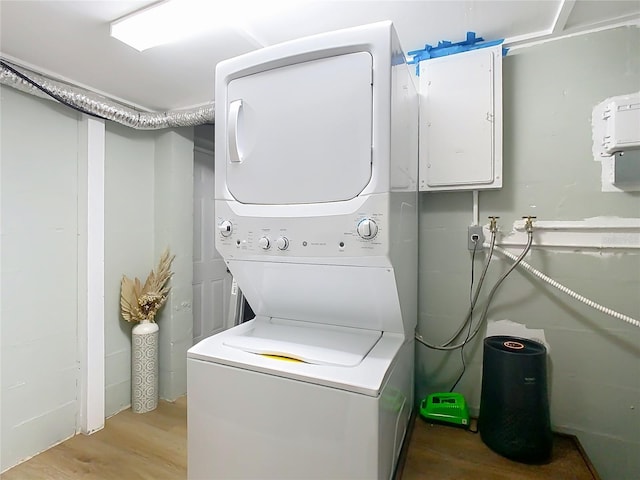 clothes washing area featuring wood finished floors, stacked washer and clothes dryer, electric panel, and laundry area