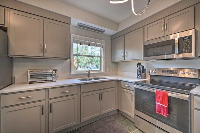 kitchen with light countertops, appliances with stainless steel finishes, a sink, and gray cabinetry