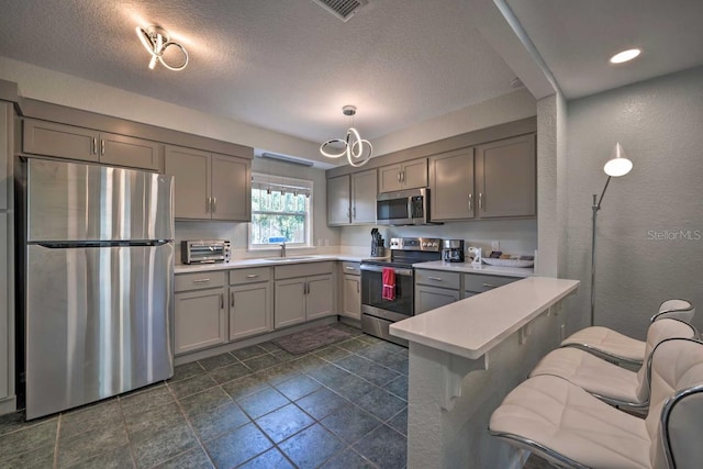 kitchen with a peninsula, gray cabinets, stainless steel appliances, light countertops, and a sink