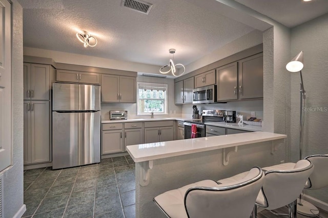 kitchen featuring light countertops, appliances with stainless steel finishes, gray cabinets, and visible vents