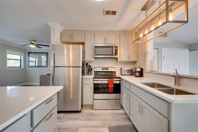 kitchen with decorative light fixtures, light wood finished floors, stainless steel appliances, visible vents, and a sink