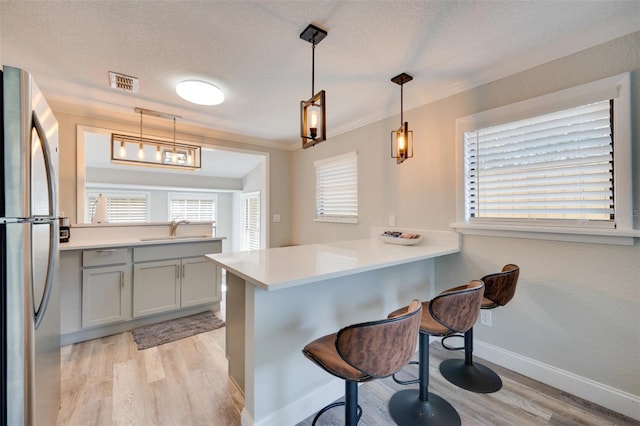 kitchen featuring a peninsula, a sink, visible vents, light wood-style floors, and freestanding refrigerator